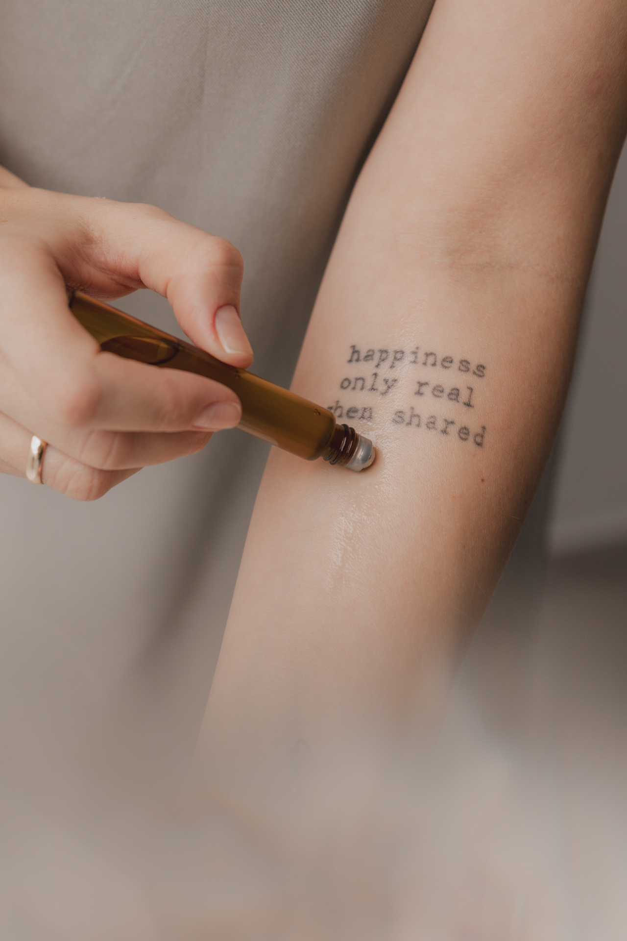 Aplicação de óleo floral no braço com tatuagem 'happiness only real when shared'